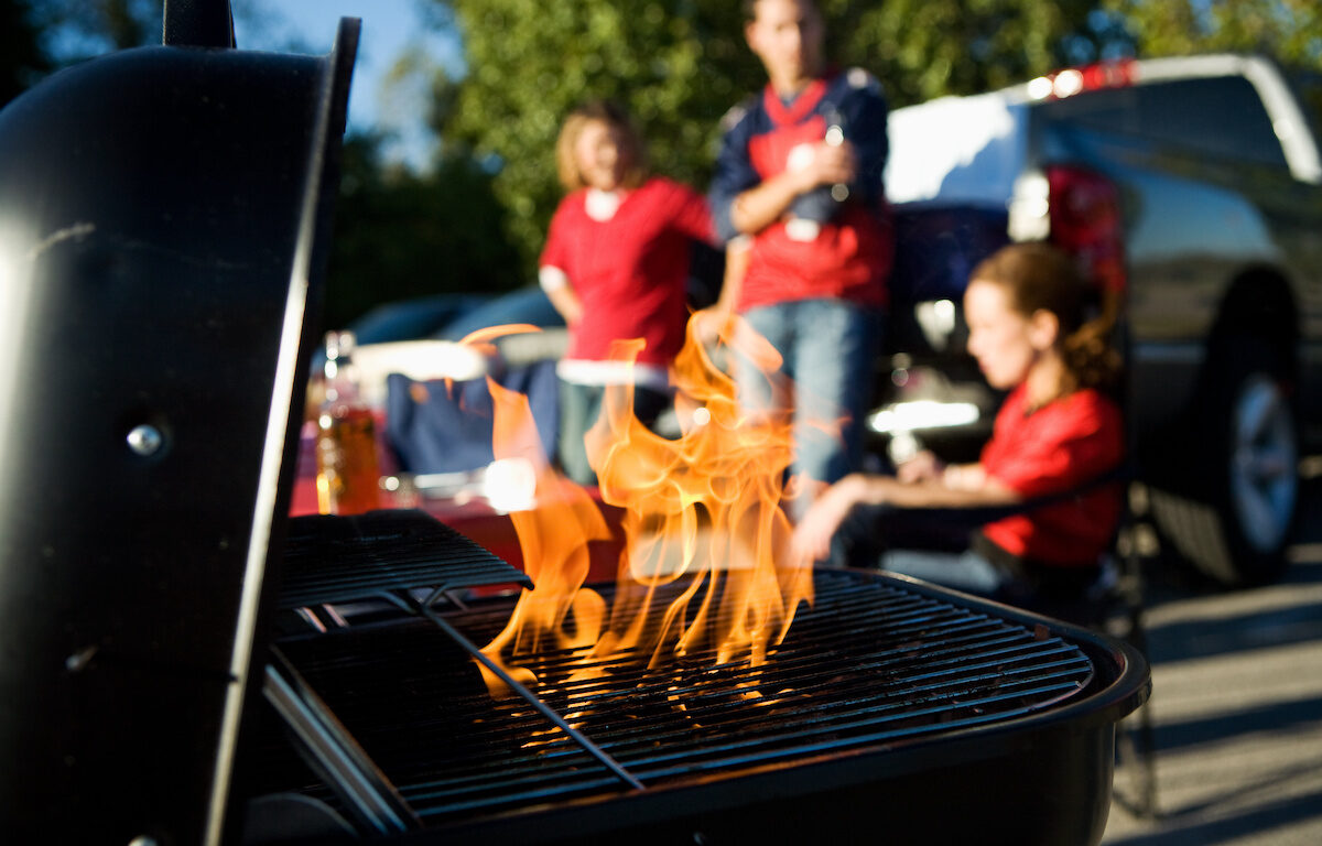 People grilling on a charcoal grill at a tailgate party before the next big football game.