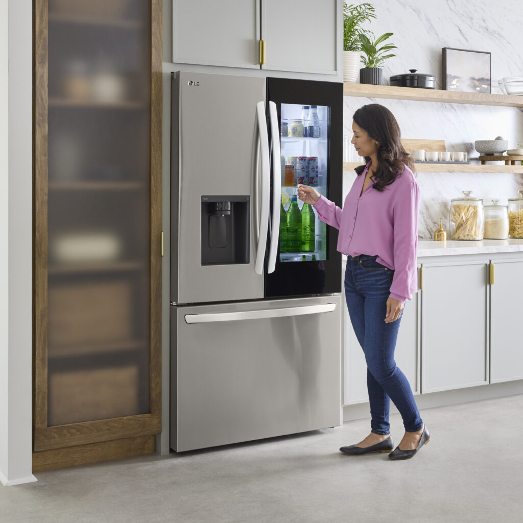 A woman going to open the external door on the LG InstaView refrigerator to get a drink.