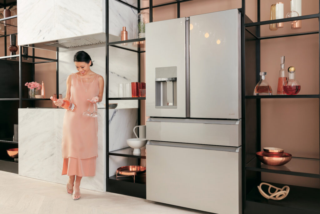 A cafe luxury french-door refrigerator with a marble gray finish in a kitchen with black shelves, and rose pink painted walls.