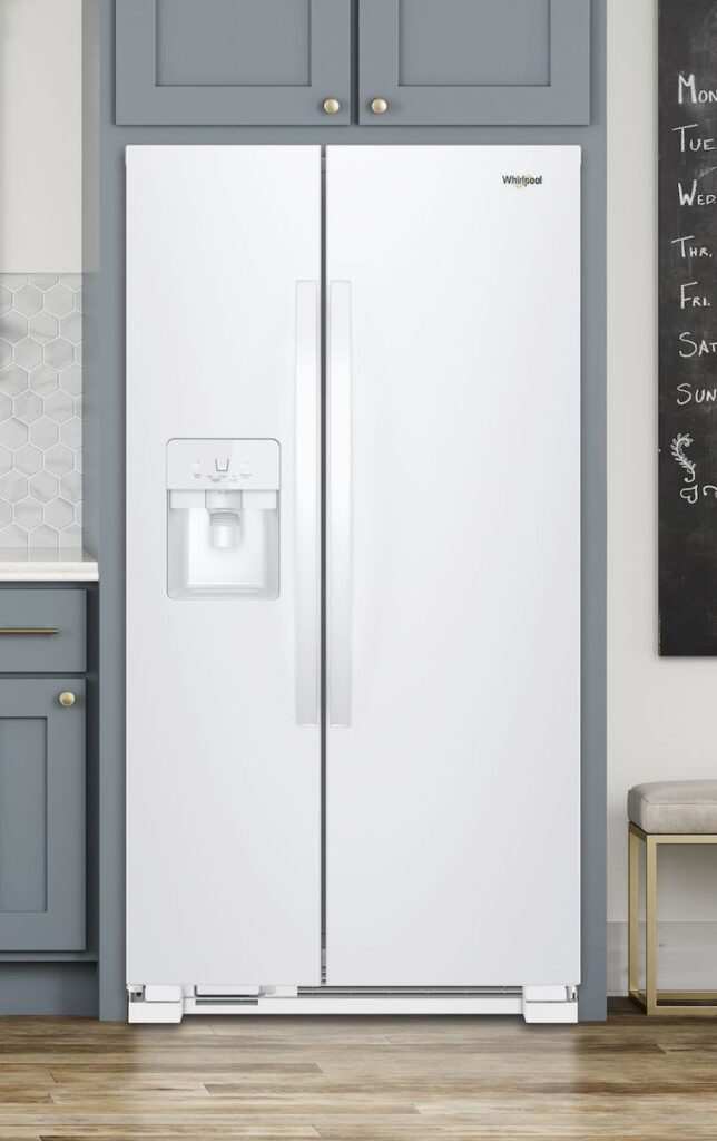 A White Whirlpool side-by-side refrigerator in a kitchen with blue-gray cabinets and part of a chalkboard visible on the right side of the image.