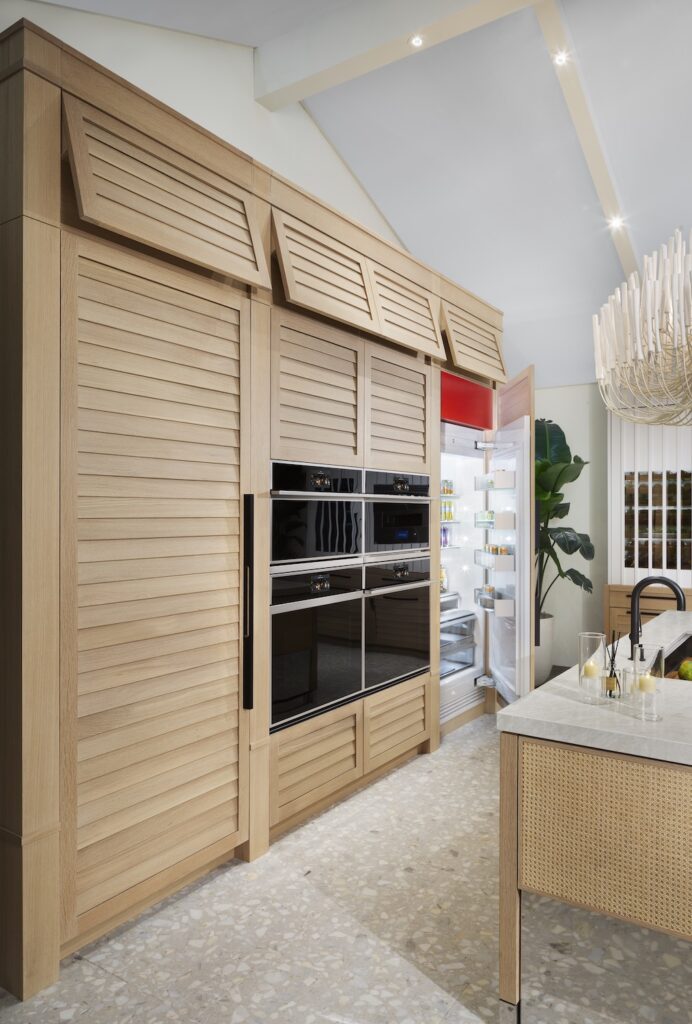 A beach house kitchen with built-in shutter-style cabinets, and an open column refrigerator. 