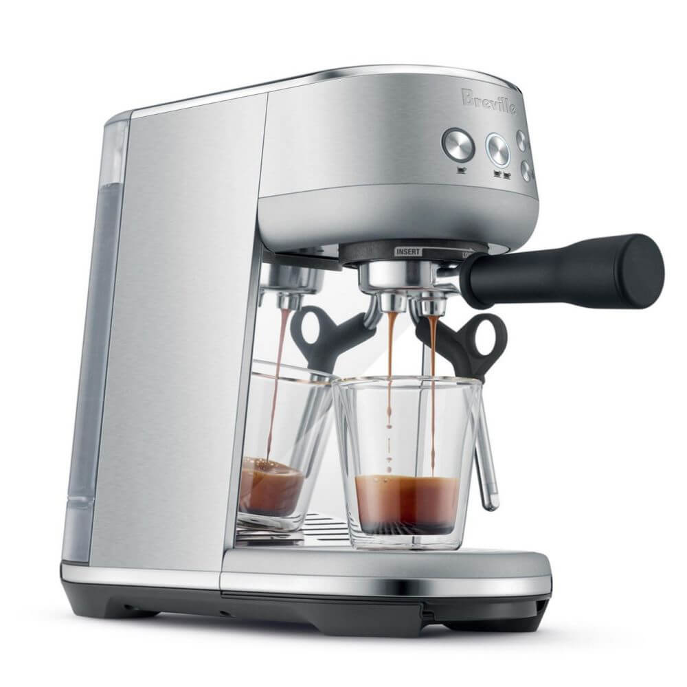 Breville stainless steel espresso maker making a small glass of espresso.