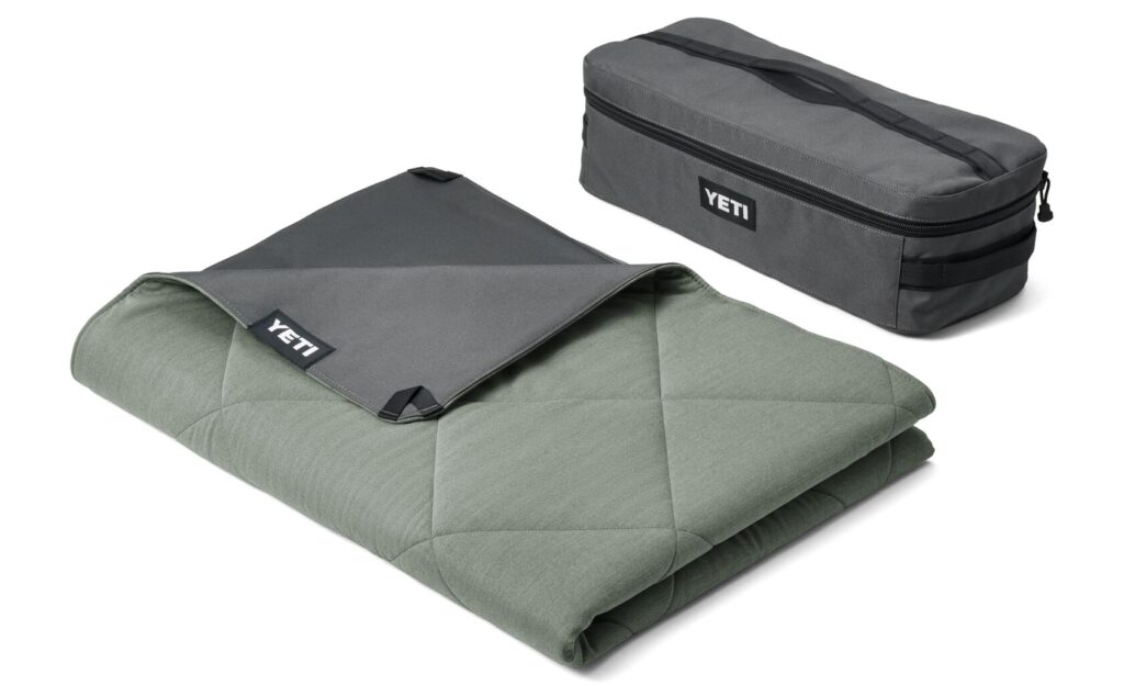 The forest green YETI Lowlands blanket sitting folded next to the blanket's carrying case.