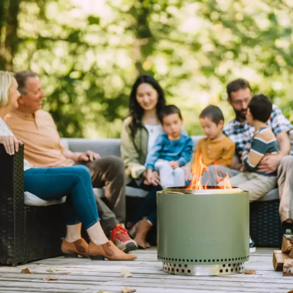 A family sitting around a portable firepit on the back deck of their home.
