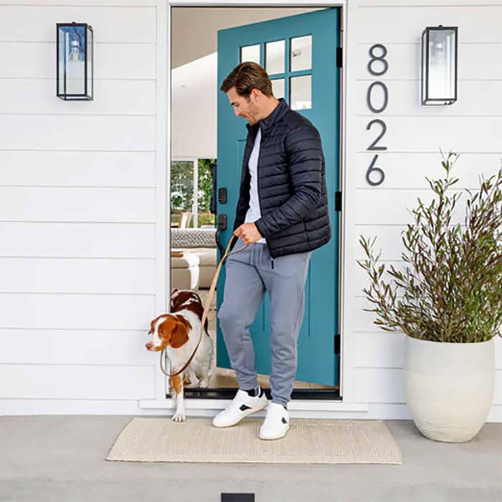 Man walking his dog out of the front door. On the door, a Yale smart lock can be seen.