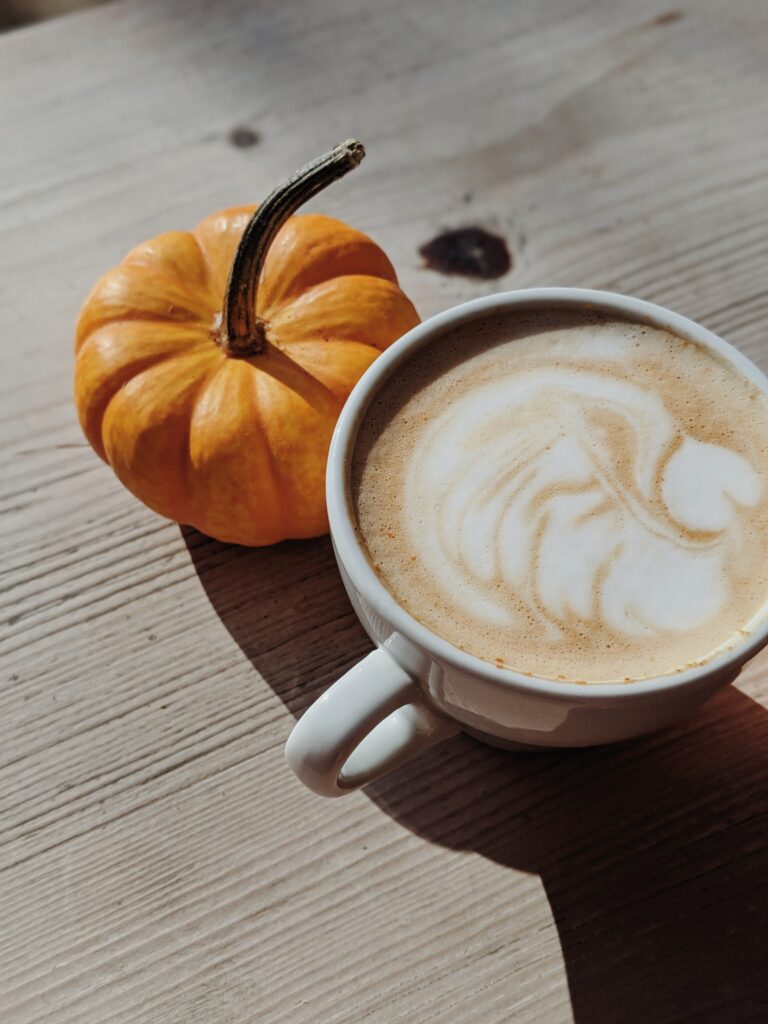 Mug of chai tea latte with hot steamed milk stands next to a small pumpkin.