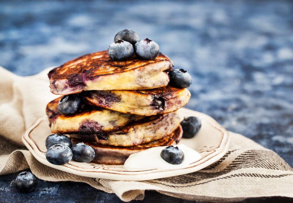 Blueberry pancakes stacked on a small plate on a blue background.