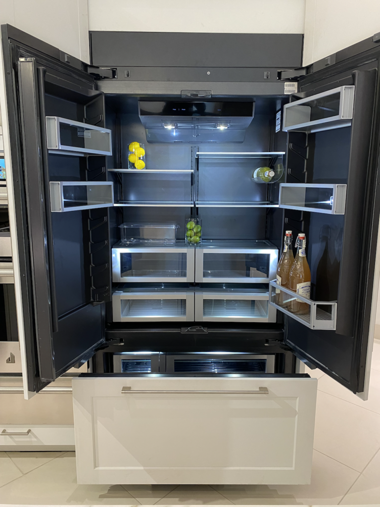 A JennAir custom panel refrigerator with its doors open showing the internal obsidian lining and LED lights.
