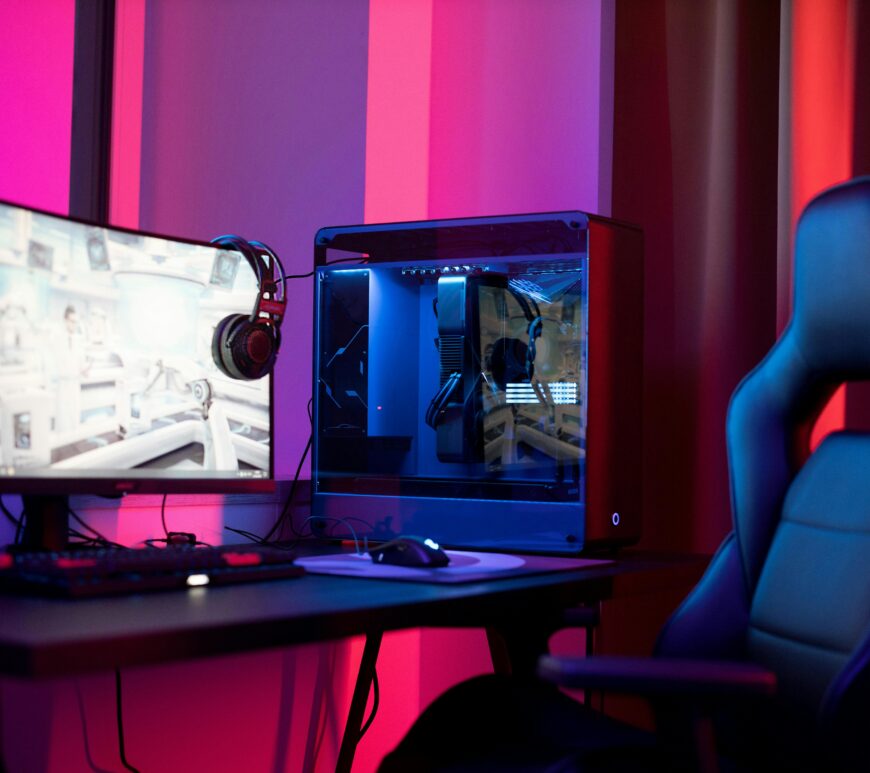 Desk set up for PC gaming in a room lit by purple, red, and magenta lights.