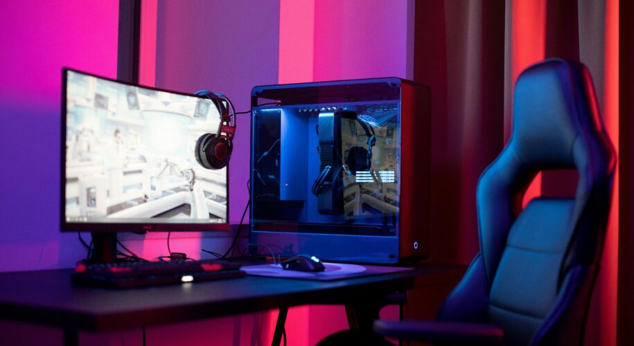 Desk set up for PC gaming in a room lit by purple, red, and magenta lights.