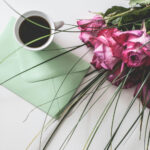 A collection of Mother's Day gifts: a cup of coffee, a bouquet of pink roses, and a card in a light green envelope.