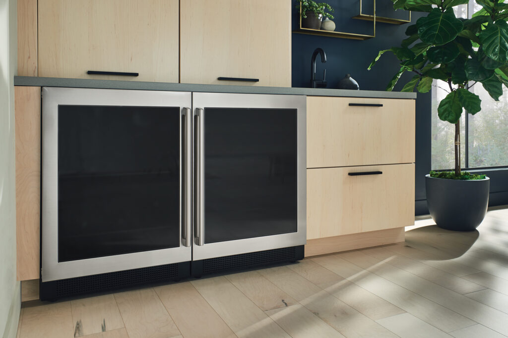 Two Electrolux beverage coolers installed side-by-side surrounded by pale brown wood cabinetry with black metal handles.